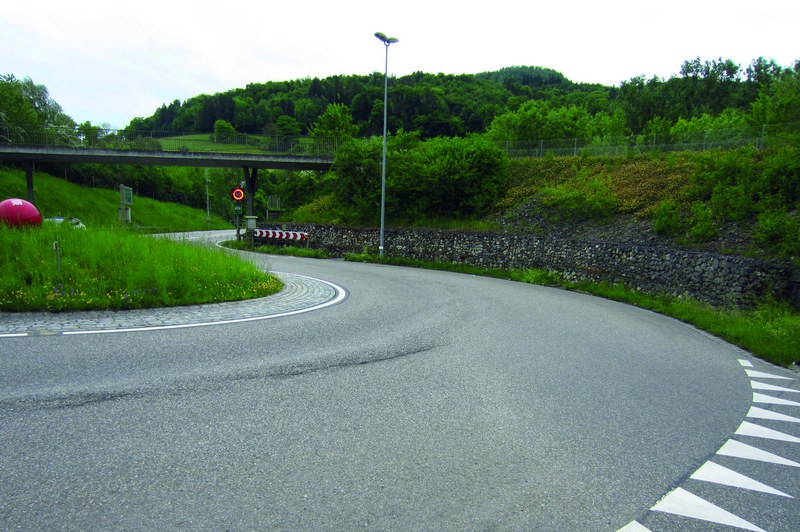 Kreisel mit Grünflächen, einer Fussgängerbrücke und bewaldeten Hügeln im Hintergrund