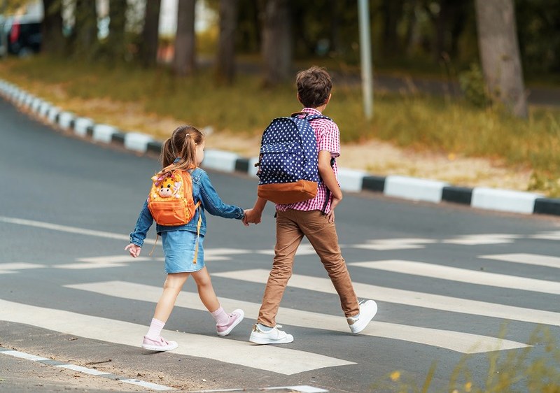 Mädchen und Junge aus der Primarschule überqueren Hand in Hand einen Zebrastreifen