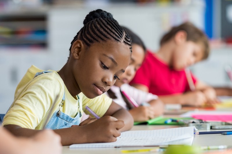 Eine sitzende Primarschülerin im Fokus, die konzentriert ein Arbeitsblatt bearbeitet