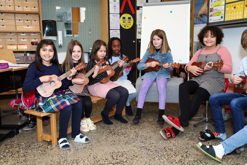Mehrere Mädchen in der Primarschulen spielen im Kreis sitzend auf Ukulelen